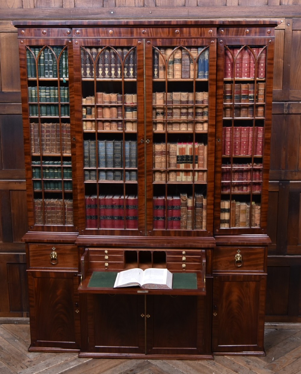 A large 19th-century flame mahogany secretaire bookcase featuring four glazed upper doors with arched astragal glazing, above a drop-down desk compartment fitted with drawers and a green writing surface.
