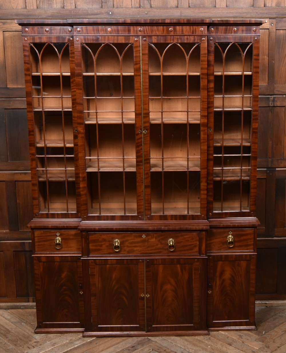 A large 19th-century flame mahogany secretaire bookcase featuring four glazed upper doors with arched astragal glazing, above a drop-down desk compartment fitted with drawers and a green writing surface. View V