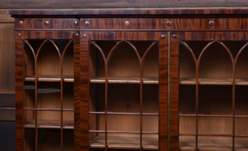 A large 19th-century flame mahogany secretaire bookcase featuring four glazed upper doors with arched astragal glazing, above a drop-down desk compartment fitted with drawers and a green writing surface. View VI