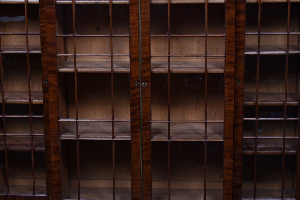 A large 19th-century flame mahogany secretaire bookcase featuring four glazed upper doors with arched astragal glazing, above a drop-down desk compartment fitted with drawers and a green writing surface. View VII