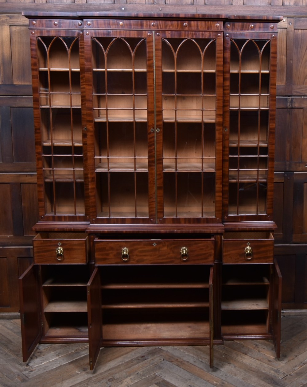 A large 19th-century flame mahogany secretaire bookcase featuring four glazed upper doors with arched astragal glazing, above a drop-down desk compartment fitted with drawers and a green writing surface. View XI