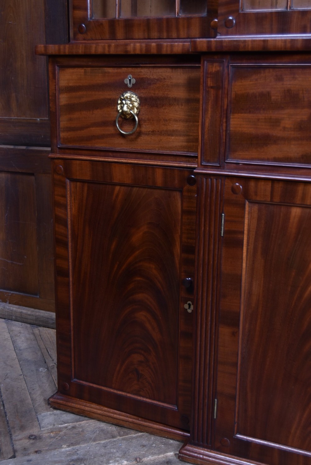 A large 19th-century flame mahogany secretaire bookcase featuring four glazed upper doors with arched astragal glazing, above a drop-down desk compartment fitted with drawers and a green writing surface. View XV
