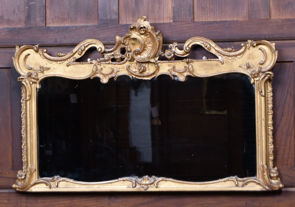 A wide Rococo style horizontal overmantel mirror with an ornate carved giltwood frame featuring an asymmetrical crest and C-scroll motifs.