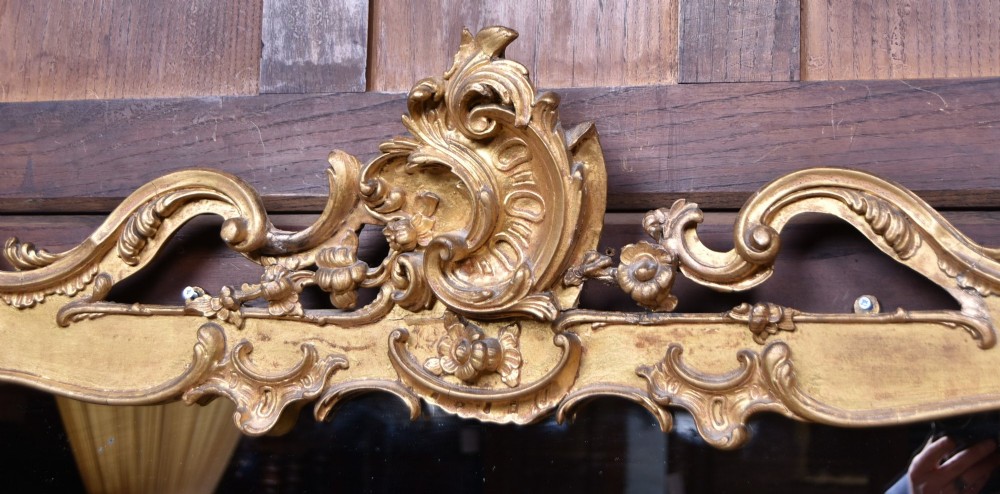 A wide Rococo style horizontal overmantel mirror with an ornate carved giltwood frame featuring an asymmetrical crest and C-scroll motifs. View III