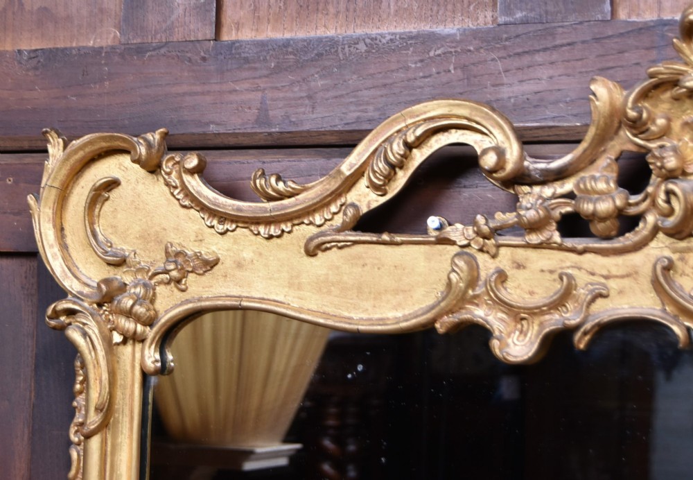 A wide Rococo style horizontal overmantel mirror with an ornate carved giltwood frame featuring an asymmetrical crest and C-scroll motifs. View IV