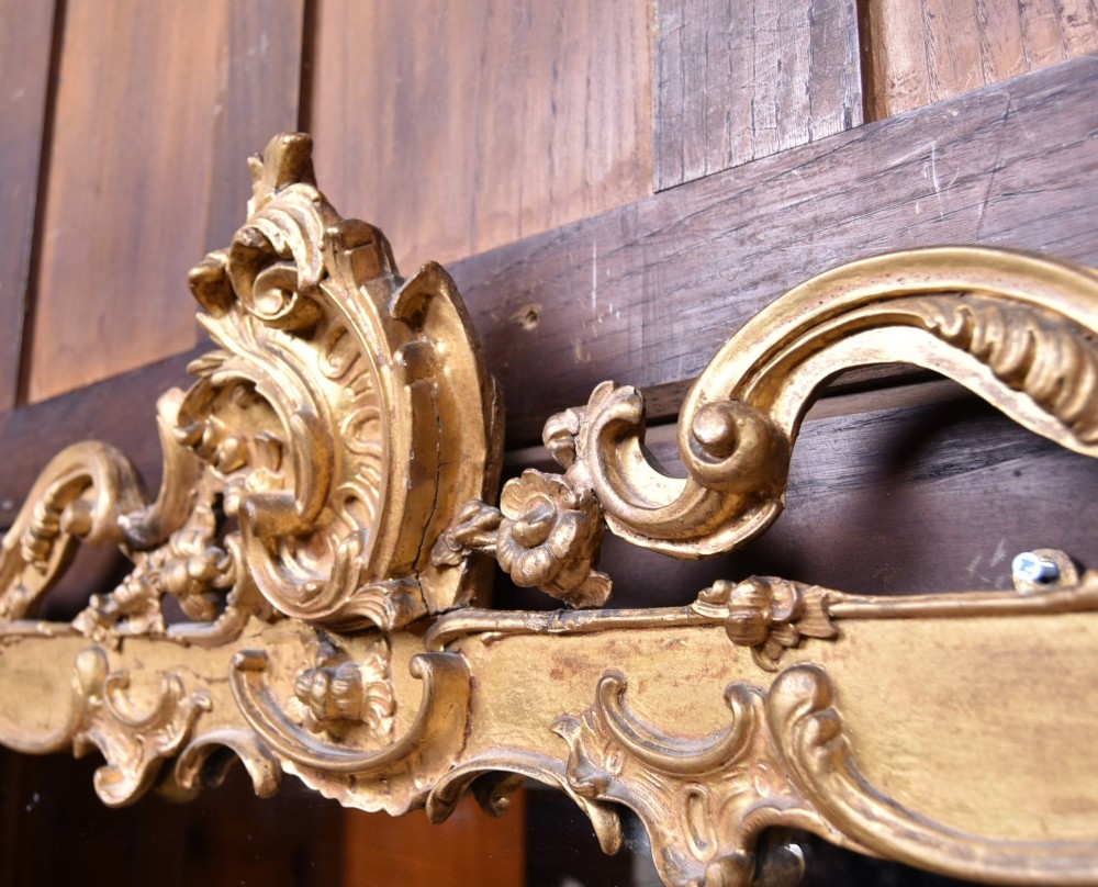 A wide Rococo style horizontal overmantel mirror with an ornate carved giltwood frame featuring an asymmetrical crest and C-scroll motifs. View IX