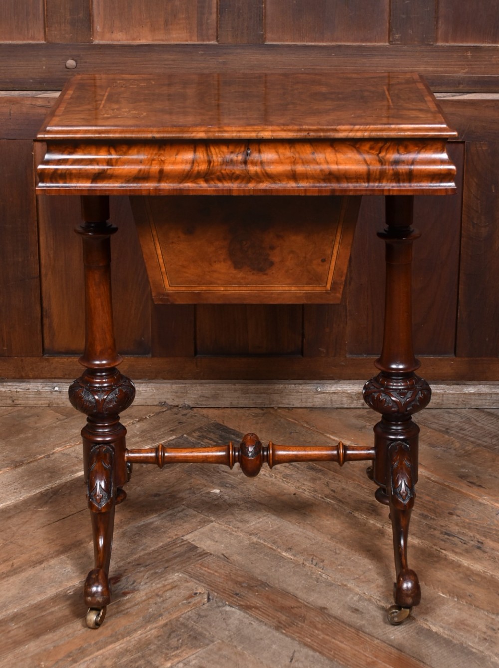 A Victorian walnut work table featuring a burr walnut top, suspended storage well beneath, double turned column supports, carved feet, and brass castors. View II