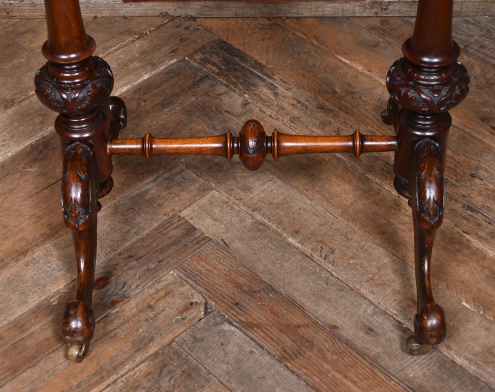 A Victorian walnut work table featuring a burr walnut top, suspended storage well beneath, double turned column supports, carved feet, and brass castors. View III