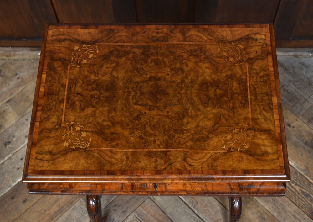 A Victorian walnut work table featuring a burr walnut top, suspended storage well beneath, double turned column supports, carved feet, and brass castors. View IV