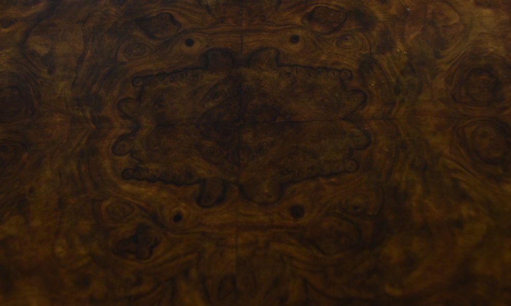 A Victorian walnut work table featuring a burr walnut top, suspended storage well beneath, double turned column supports, carved feet, and brass castors. View VII