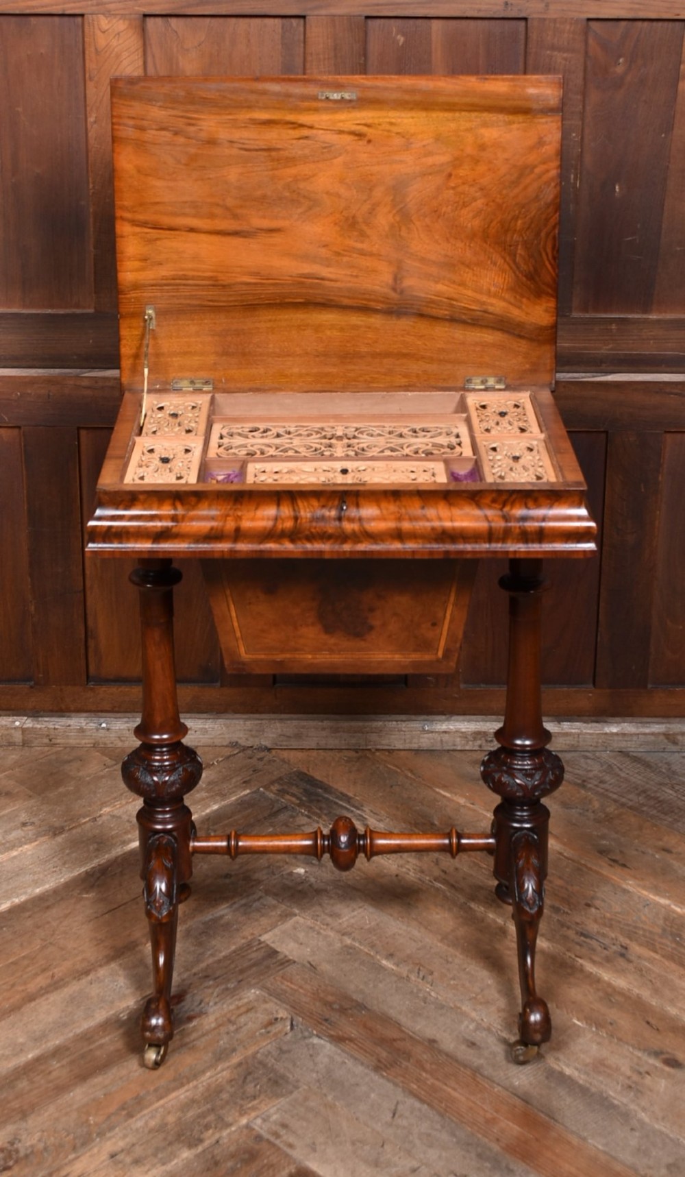 A Victorian walnut work table featuring a burr walnut top, suspended storage well beneath, double turned column supports, carved feet, and brass castors. View VIII