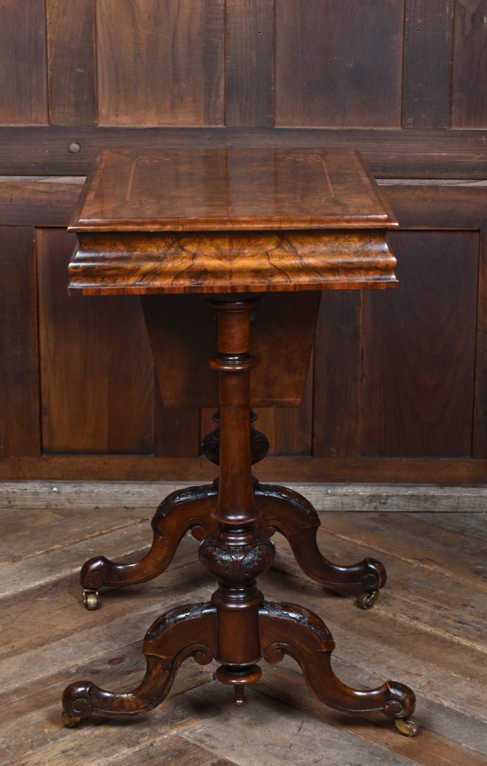 A Victorian walnut work table featuring a burr walnut top, suspended storage well beneath, double turned column supports, carved feet, and brass castors. View XI