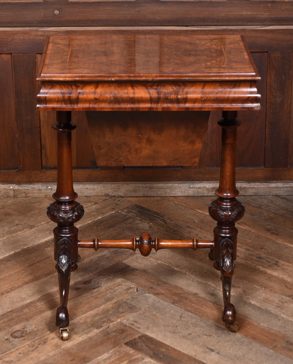A Victorian walnut work table featuring a burr walnut top, suspended storage well beneath, double turned column supports, carved feet, and brass castors. View XII