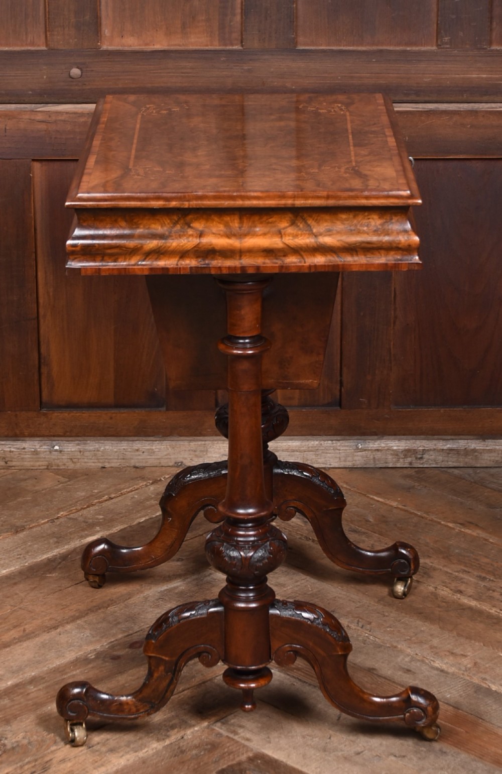 A Victorian walnut work table featuring a burr walnut top, suspended storage well beneath, double turned column supports, carved feet, and brass castors. View XIII