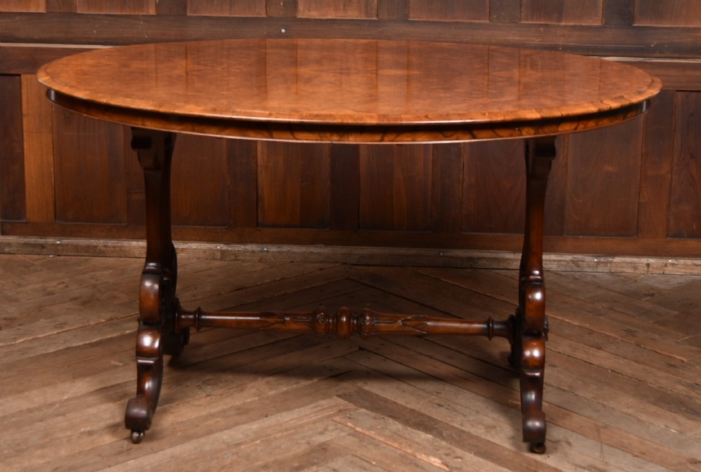 A Victorian oval centre table constructed from burr walnut, featuring carved twin pedestal legs connected by a central turned stretcher. View II