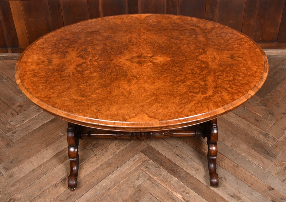 A Victorian oval centre table constructed from burr walnut, featuring carved twin pedestal legs connected by a central turned stretcher. View III