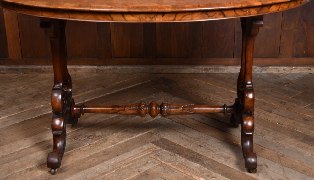 A Victorian oval centre table constructed from burr walnut, featuring carved twin pedestal legs connected by a central turned stretcher. View VII