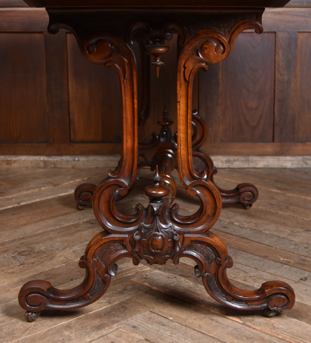 A Victorian oval centre table constructed from burr walnut, featuring carved twin pedestal legs connected by a central turned stretcher. View VIII