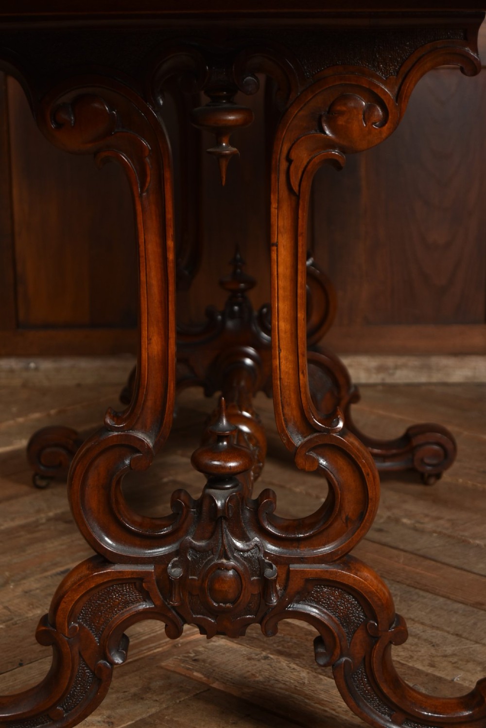 A Victorian oval centre table constructed from burr walnut, featuring carved twin pedestal legs connected by a central turned stretcher. View IX
