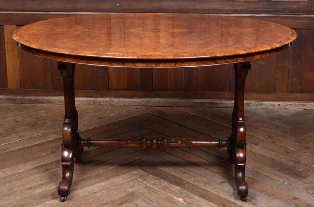 A Victorian oval centre table constructed from burr walnut, featuring carved twin pedestal legs connected by a central turned stretcher. View XI