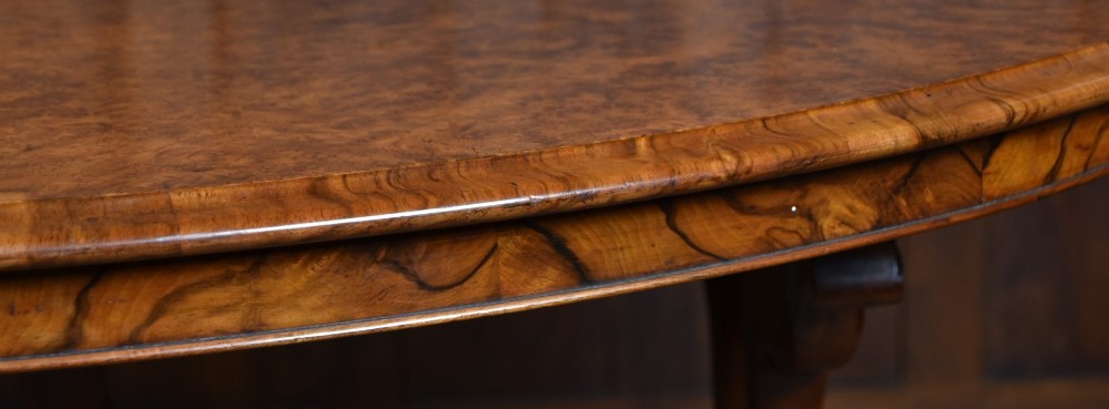 A Victorian oval centre table constructed from burr walnut, featuring carved twin pedestal legs connected by a central turned stretcher. View XIII
