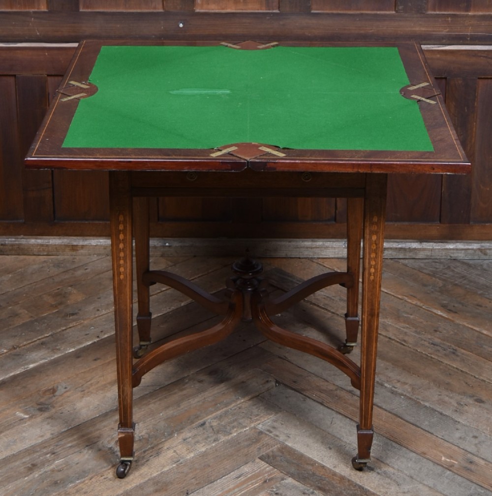 An Edwardian mahogany envelope card table featuring satinwood marquetry inlay, a single drawer, and a curved cross-stretcher with brass castors. View VII