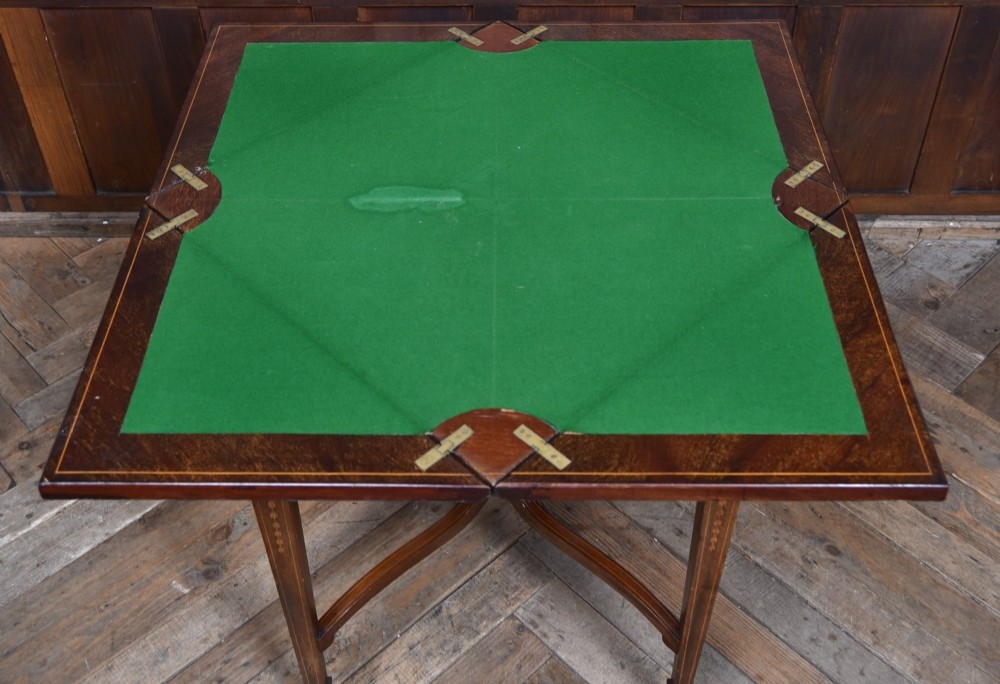 An Edwardian mahogany envelope card table featuring satinwood marquetry inlay, a single drawer, and a curved cross-stretcher with brass castors. View VIII
