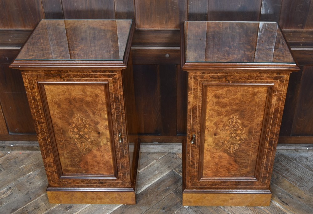A matching pair of Edwardian burr walnut bedside pot cupboards featuring central marquetry inlays, single doors, glass tops, and plinth bases. View V