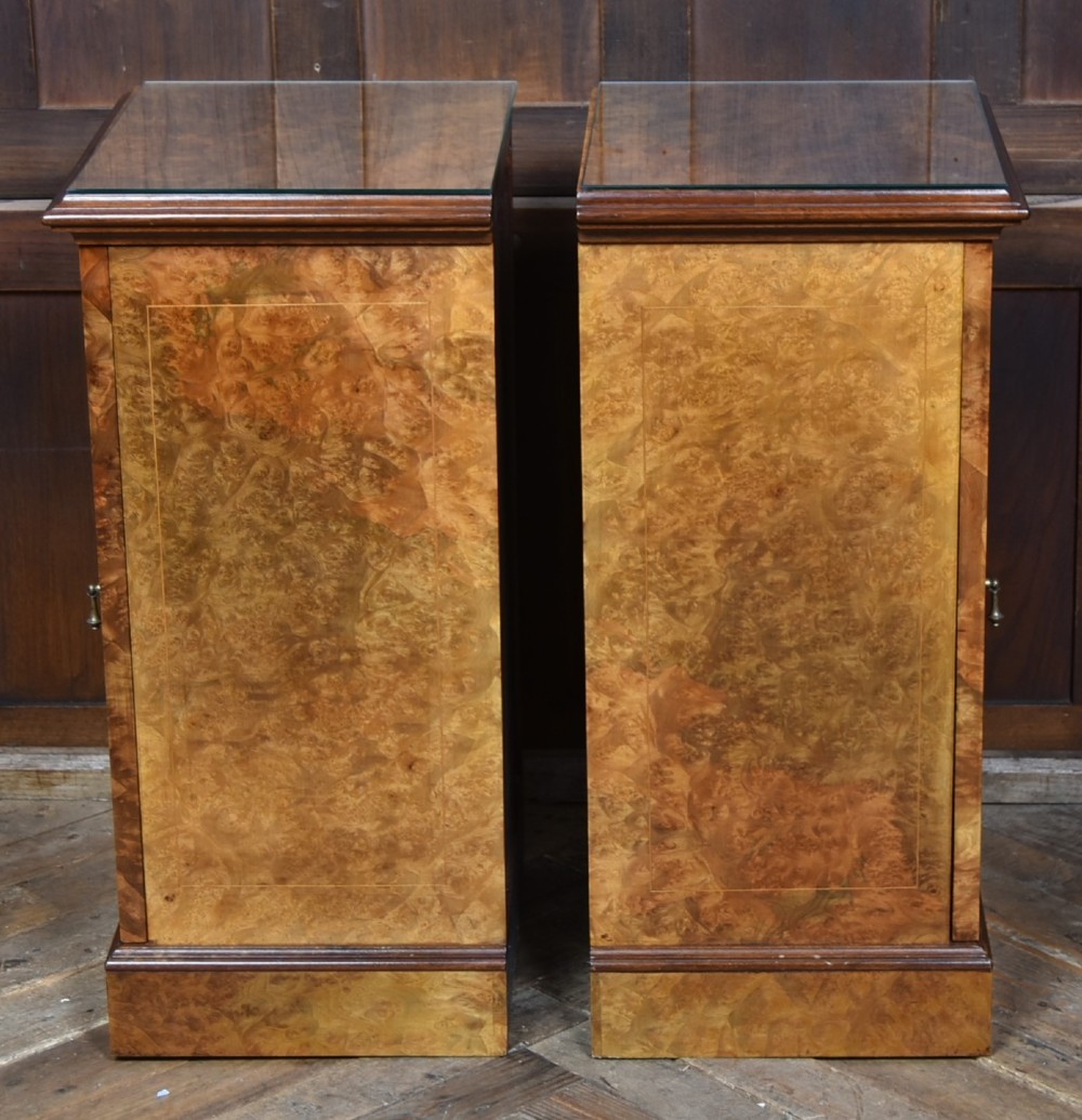 A matching pair of Edwardian burr walnut bedside pot cupboards featuring central marquetry inlays, single doors, glass tops, and plinth bases. View VII