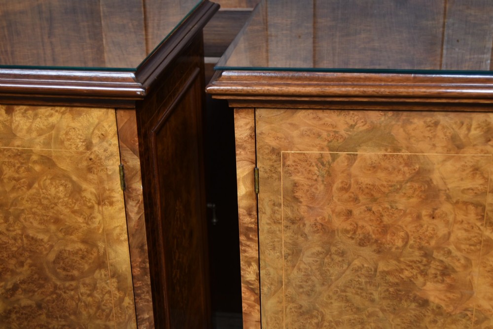 A matching pair of Edwardian burr walnut bedside pot cupboards featuring central marquetry inlays, single doors, glass tops, and plinth bases. View X