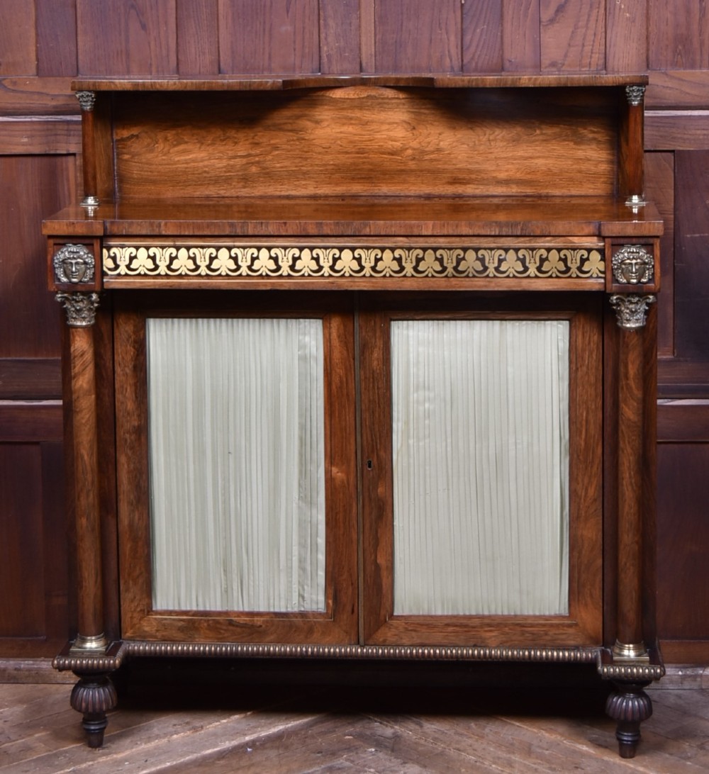A Victorian dark rosewood chiffonier cabinet featuring a decorative brass inlay border, brass mask accents, two pleated silk fabric door panels, turned feet, and a raised upper tier shelf. View II