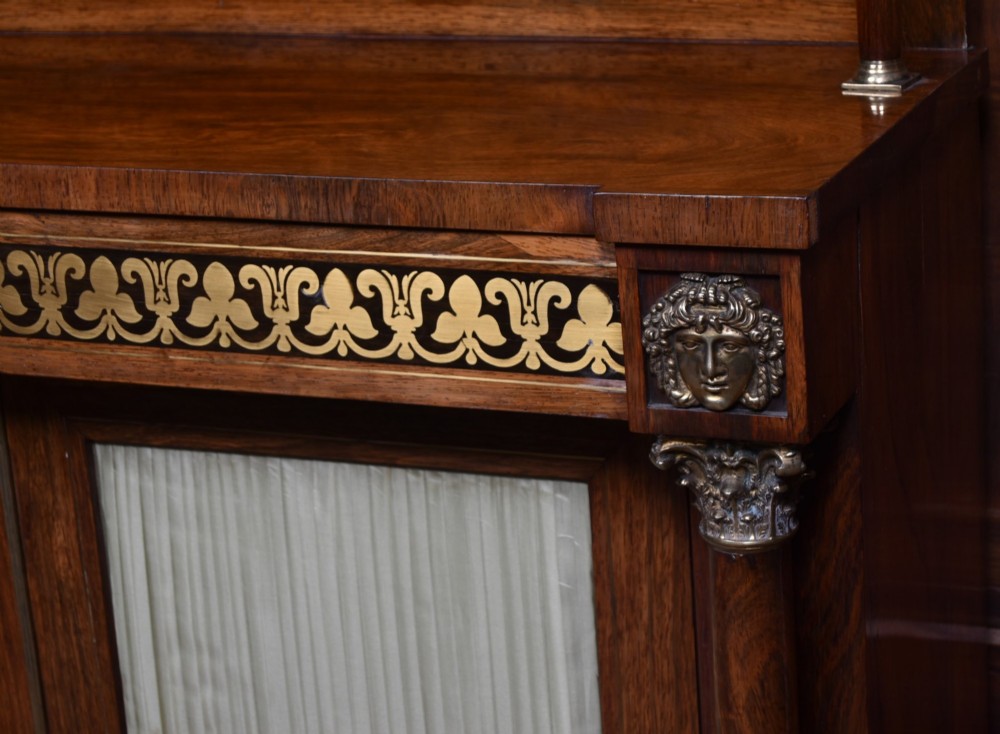 A Victorian dark rosewood chiffonier cabinet featuring a decorative brass inlay border, brass mask accents, two pleated silk fabric door panels, turned feet, and a raised upper tier shelf. View IV