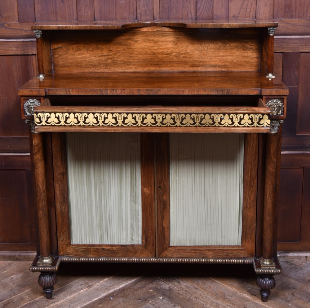 A Victorian dark rosewood chiffonier cabinet featuring a decorative brass inlay border, brass mask accents, two pleated silk fabric door panels, turned feet, and a raised upper tier shelf. View VII
