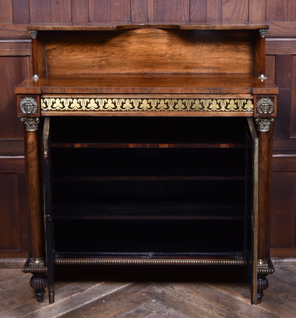 A Victorian dark rosewood chiffonier cabinet featuring a decorative brass inlay border, brass mask accents, two pleated silk fabric door panels, turned feet, and a raised upper tier shelf. View VIII