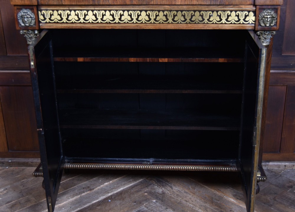 A Victorian dark rosewood chiffonier cabinet featuring a decorative brass inlay border, brass mask accents, two pleated silk fabric door panels, turned feet, and a raised upper tier shelf. View IX