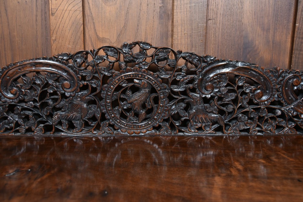 A dark hand-carved wooden demi-lune console table with intricate foliage openwork, carved lion mask legs, and a fitted glass top. View III