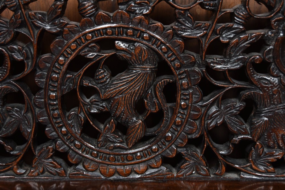 A dark hand-carved wooden demi-lune console table with intricate foliage openwork, carved lion mask legs, and a fitted glass top. View IV