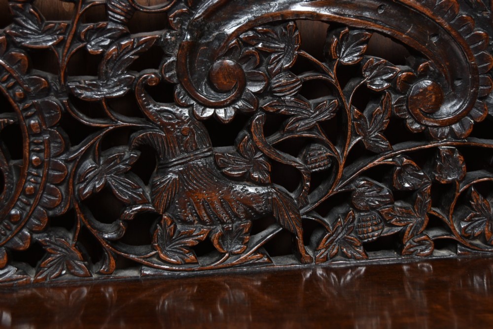 A dark hand-carved wooden demi-lune console table with intricate foliage openwork, carved lion mask legs, and a fitted glass top. View V