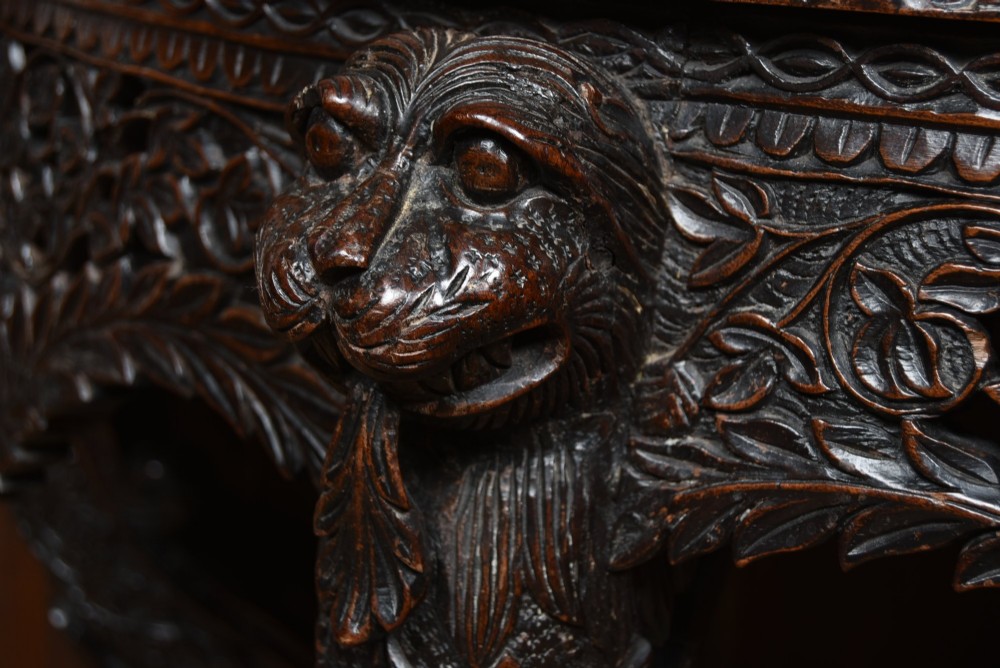 A dark hand-carved wooden demi-lune console table with intricate foliage openwork, carved lion mask legs, and a fitted glass top. View VI