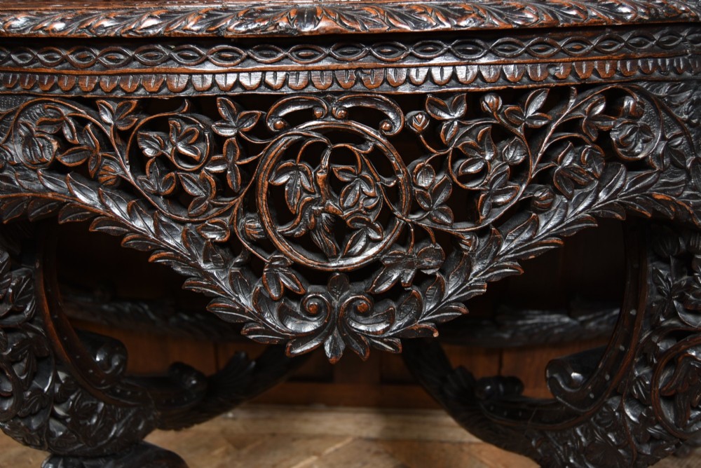 A dark hand-carved wooden demi-lune console table with intricate foliage openwork, carved lion mask legs, and a fitted glass top. View VII