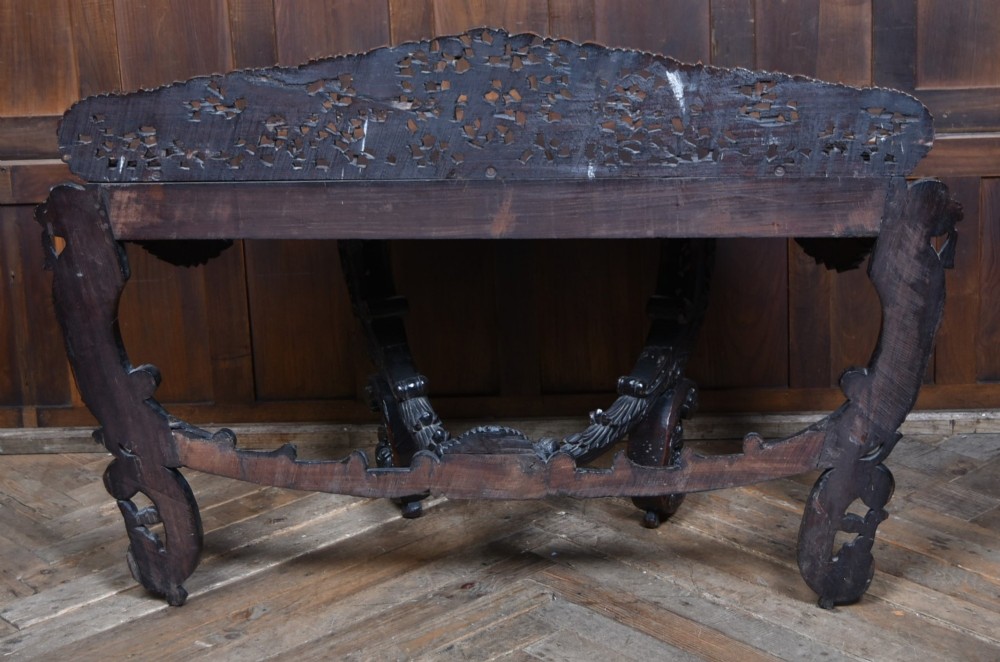 A dark hand-carved wooden demi-lune console table with intricate foliage openwork, carved lion mask legs, and a fitted glass top. View XIV