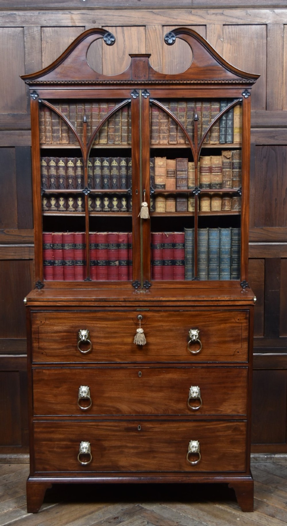 An early nineteenth-century mahogany secretaire bookcase featuring a swan-neck pediment, astragal glazed upper doors, and a lower chest of drawers with brass lion-head handles.