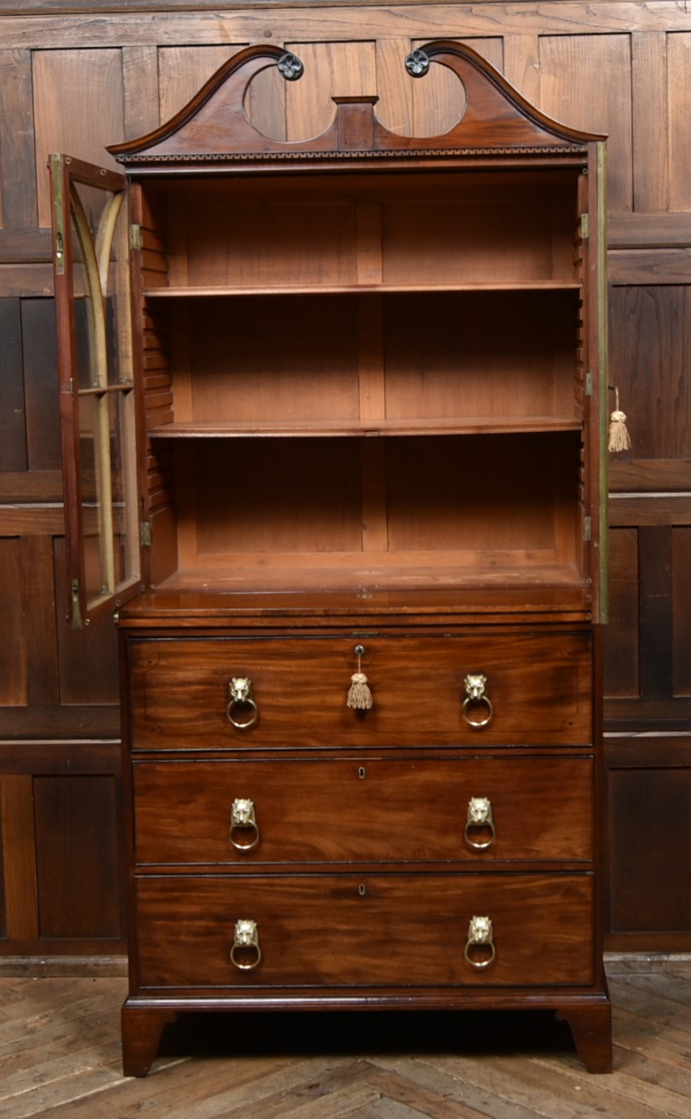 An early nineteenth-century mahogany secretaire bookcase featuring a swan-neck pediment, astragal glazed upper doors, and a lower chest of drawers with brass lion-head handles. View V