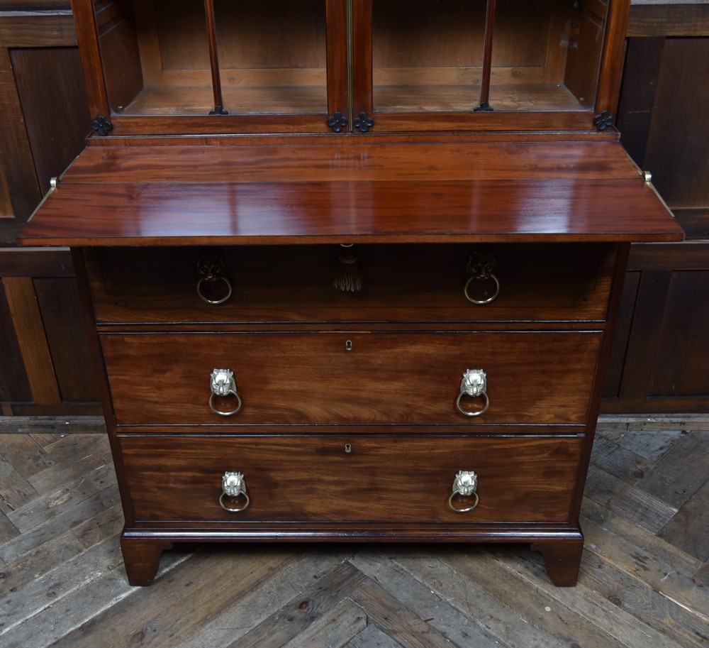 An early nineteenth-century mahogany secretaire bookcase featuring a swan-neck pediment, astragal glazed upper doors, and a lower chest of drawers with brass lion-head handles. View VI