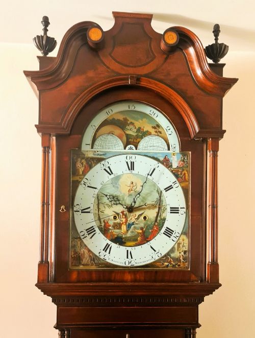 fig 1. A late 18th-century Georgian mahogany longcase clock featuring a swan-neck pediment, a painted arch dial with moon phase indicator, and a gothic shaped trunk door.