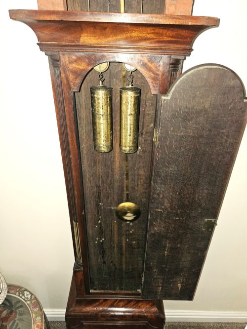 fig 1. A Georgian flame mahogany longcase clock featuring an arched hood with brass-capped fluted columns, an engraved brass dial with Roman numerals, and a trunk door showcasing rich wood grain.