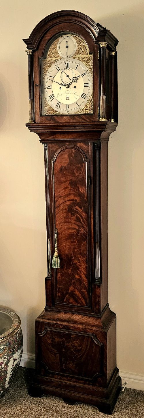 A Georgian flame mahogany longcase clock featuring an arched hood with brass-capped fluted columns, an engraved brass dial with Roman numerals, and a trunk door showcasing rich wood grain. View XIII