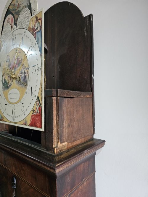 fig 6. A Regency mahogany longcase clock featuring a swan-neck pediment, a painted dial with a moonphase complication, and a Gothic arch door with flame mahogany veneers.
