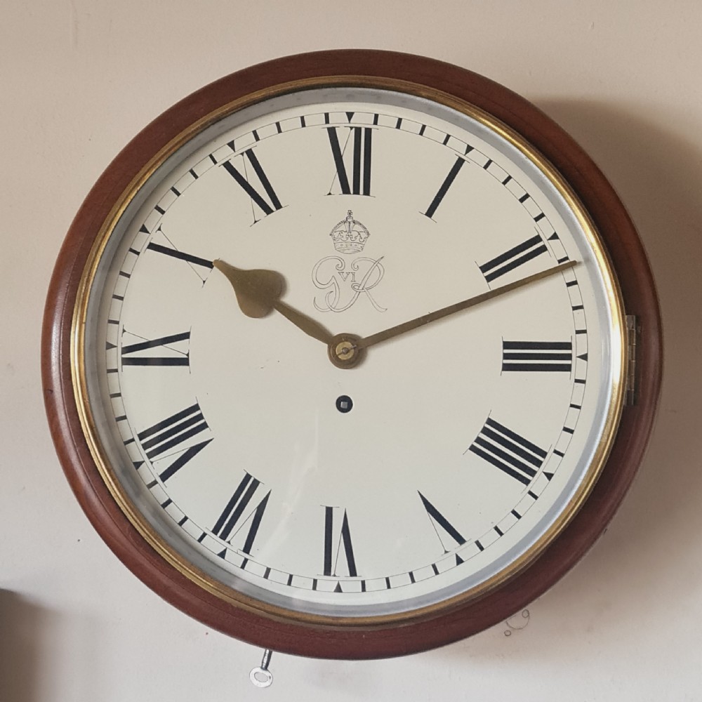 A circular wall clock with a mahogany wood frame, brass bezel, cream dial with Roman numerals, and the royal cypher of King George VI.