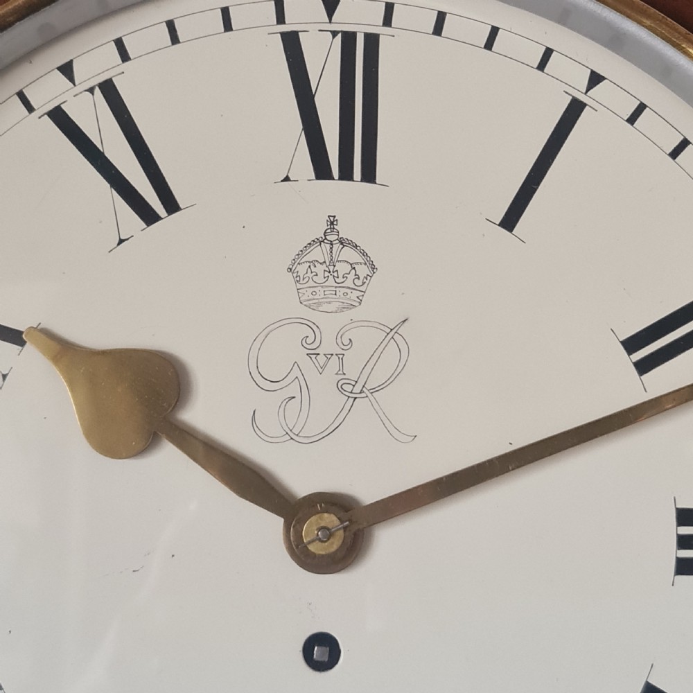 A circular wall clock with a mahogany wood frame, brass bezel, cream dial with Roman numerals, and the royal cypher of King George VI. View II